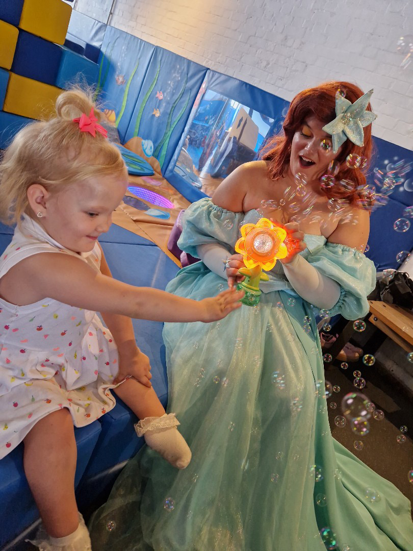 A little girl playing with a bubble wand with a mermaid character at Little Harbour Club