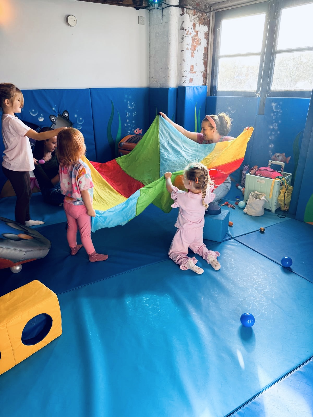 Staff and toddlers playing parachute games on the soft mats at Little Harbour Club