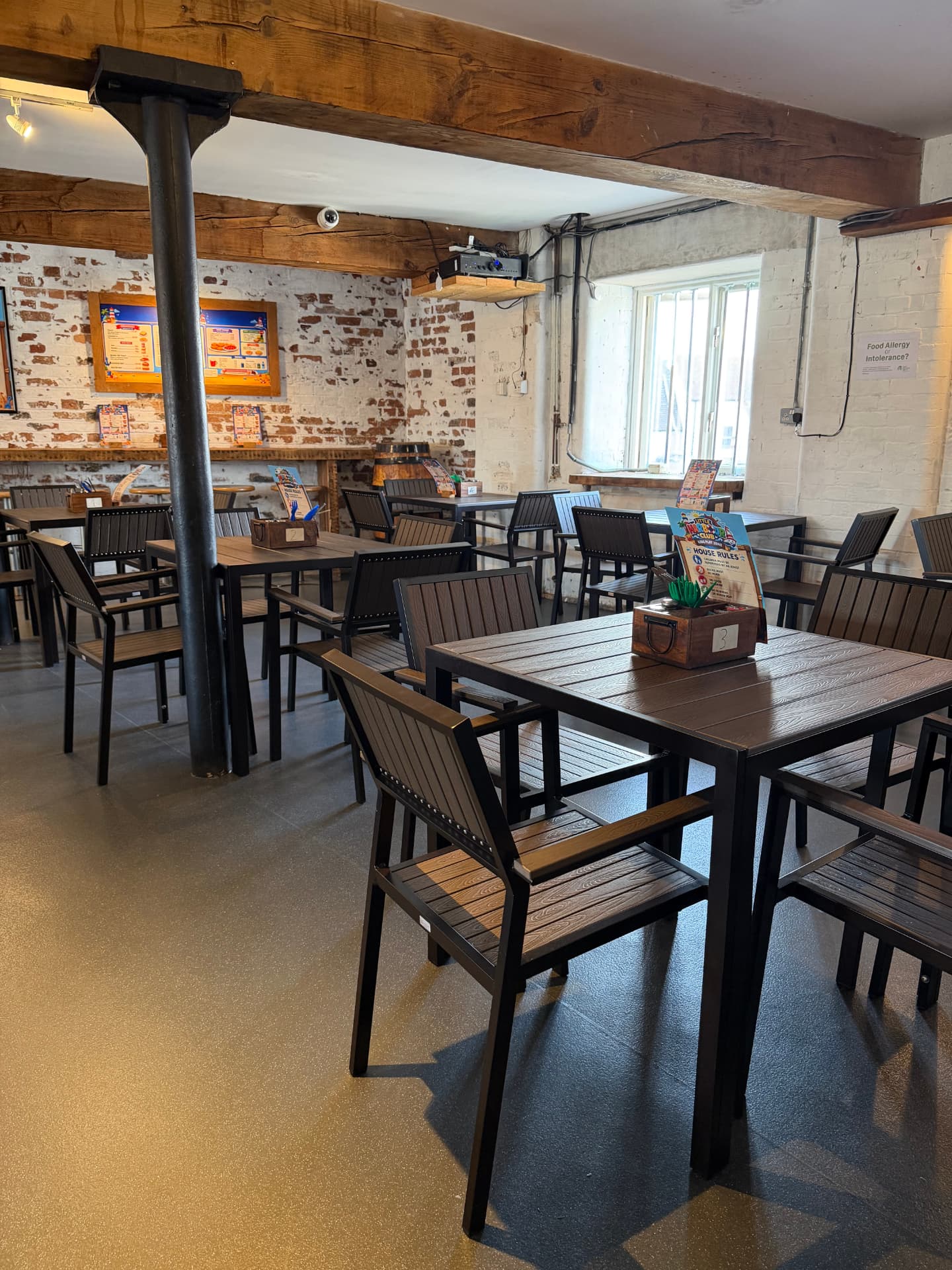 Tables and chairs in The Harbour Café at Little Harbour Club, with brick walls, wooden beams and menu boards